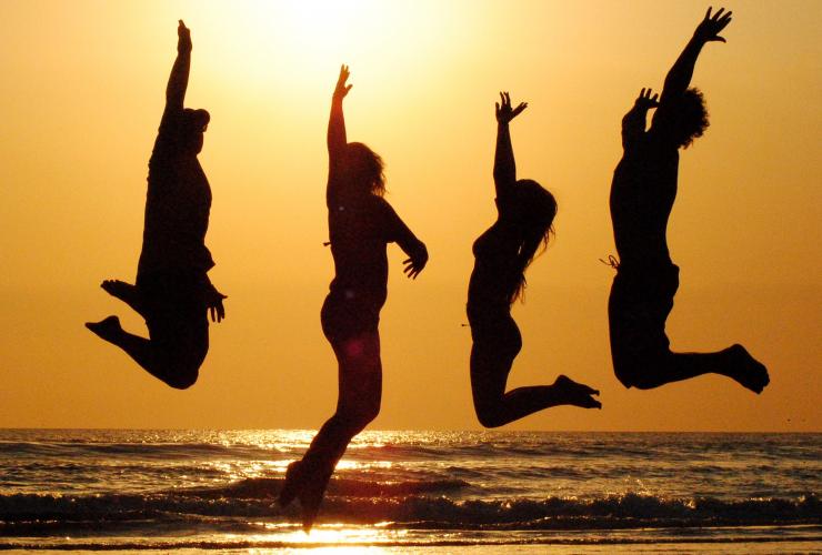 4 people jumping on the beach at sunset silhouetted