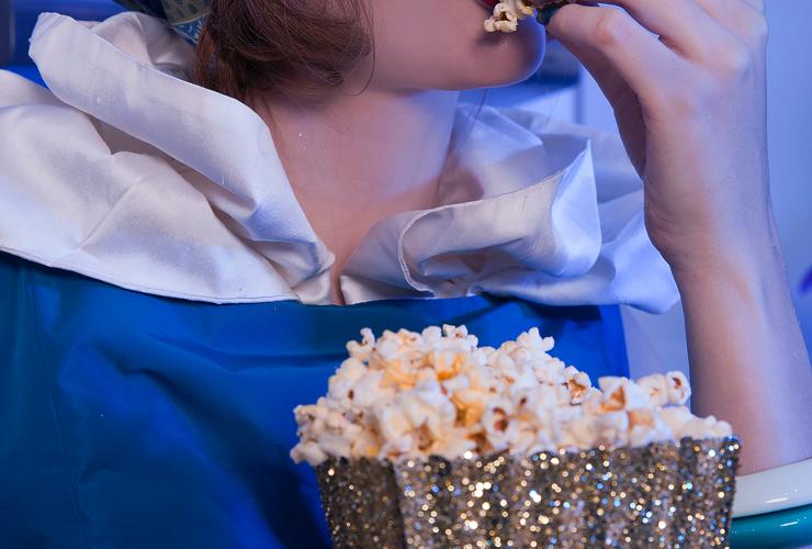 A woman with red lipstick puts popcorn in her mouth