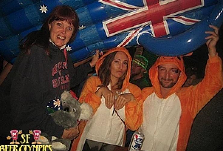 Two people in orange onesies stand next to another person holding a float with the Australia flag on it 