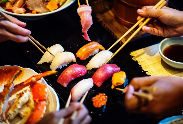 plate of sushi with hands and chopsticks 