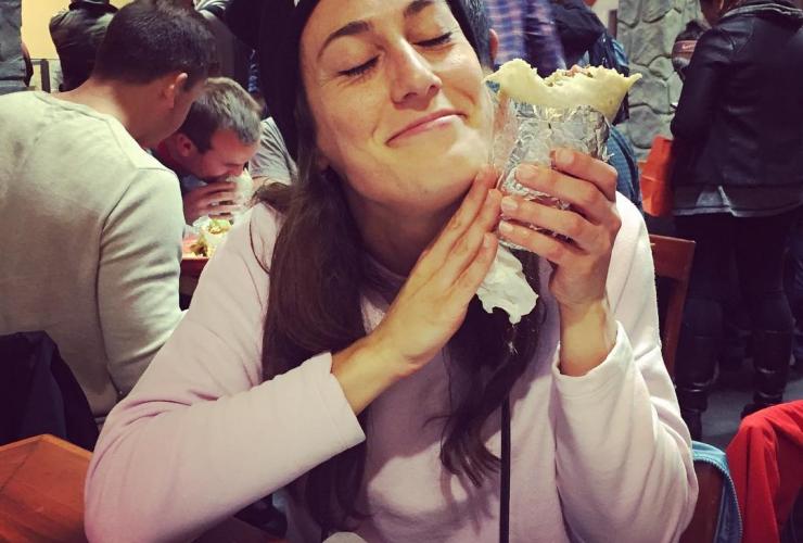 A happy woman holds a burrito up to her cheek